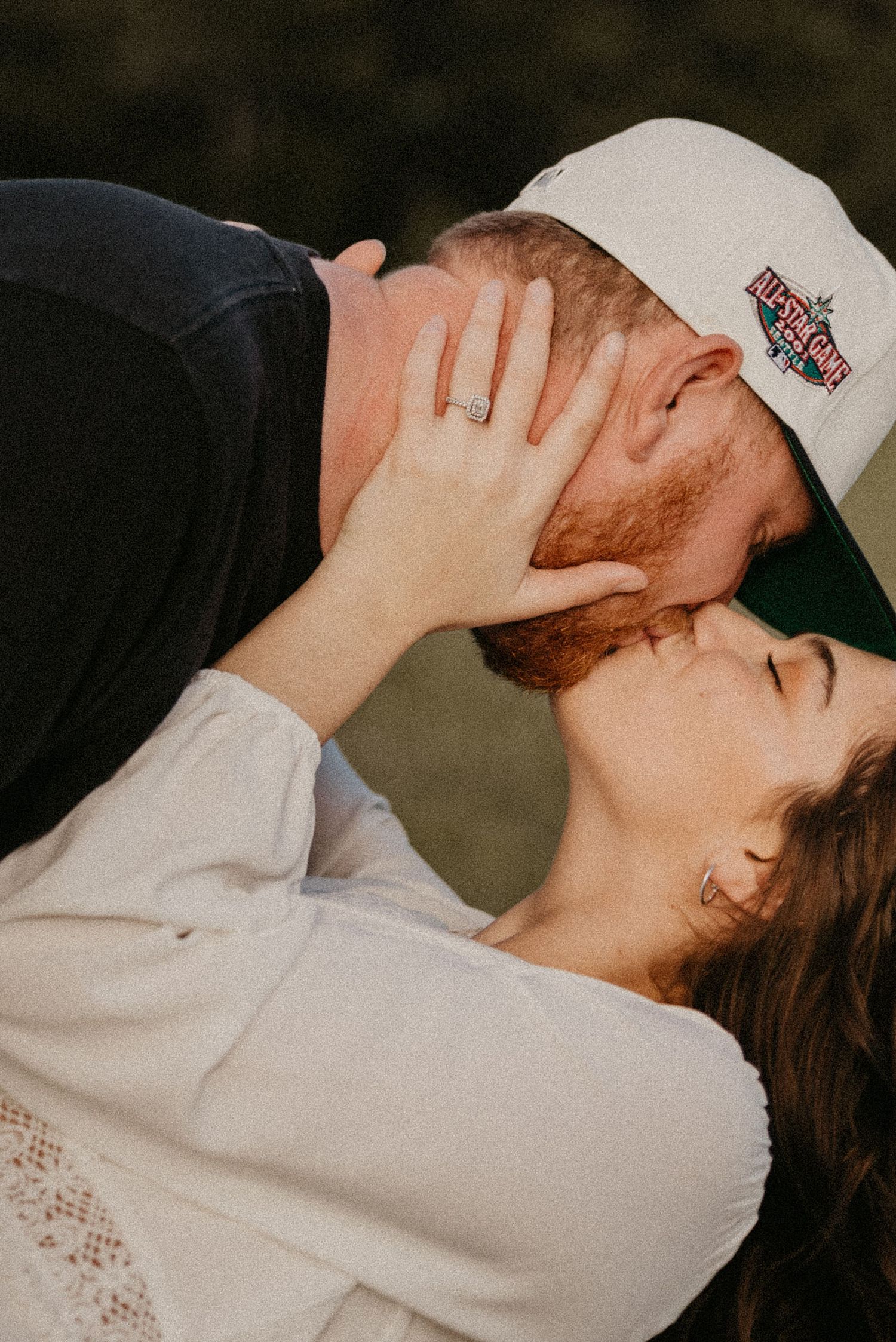 Romantic couple sharing an intimate moment outdoors with one wearing a baseball cap.