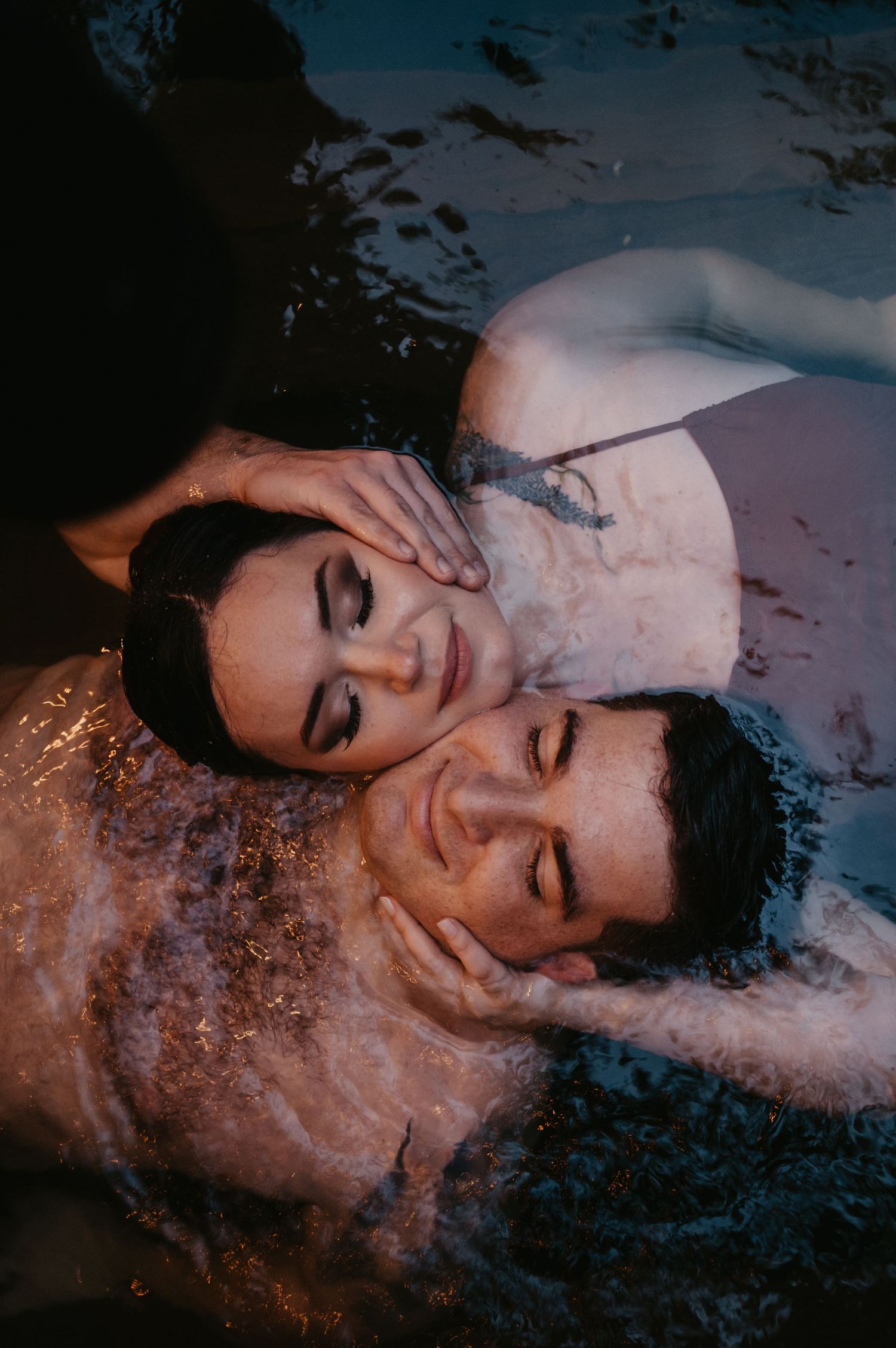 Romantic couple floating in dark water during intimate sunset photo session.