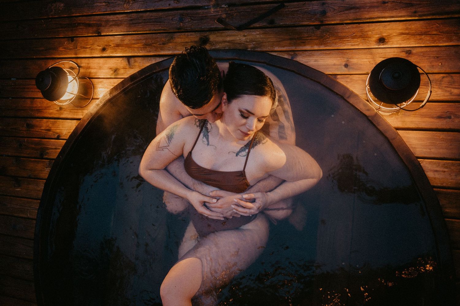 Atmospheric overhead shot of person relaxing in wooden bathtub with mood lighting.