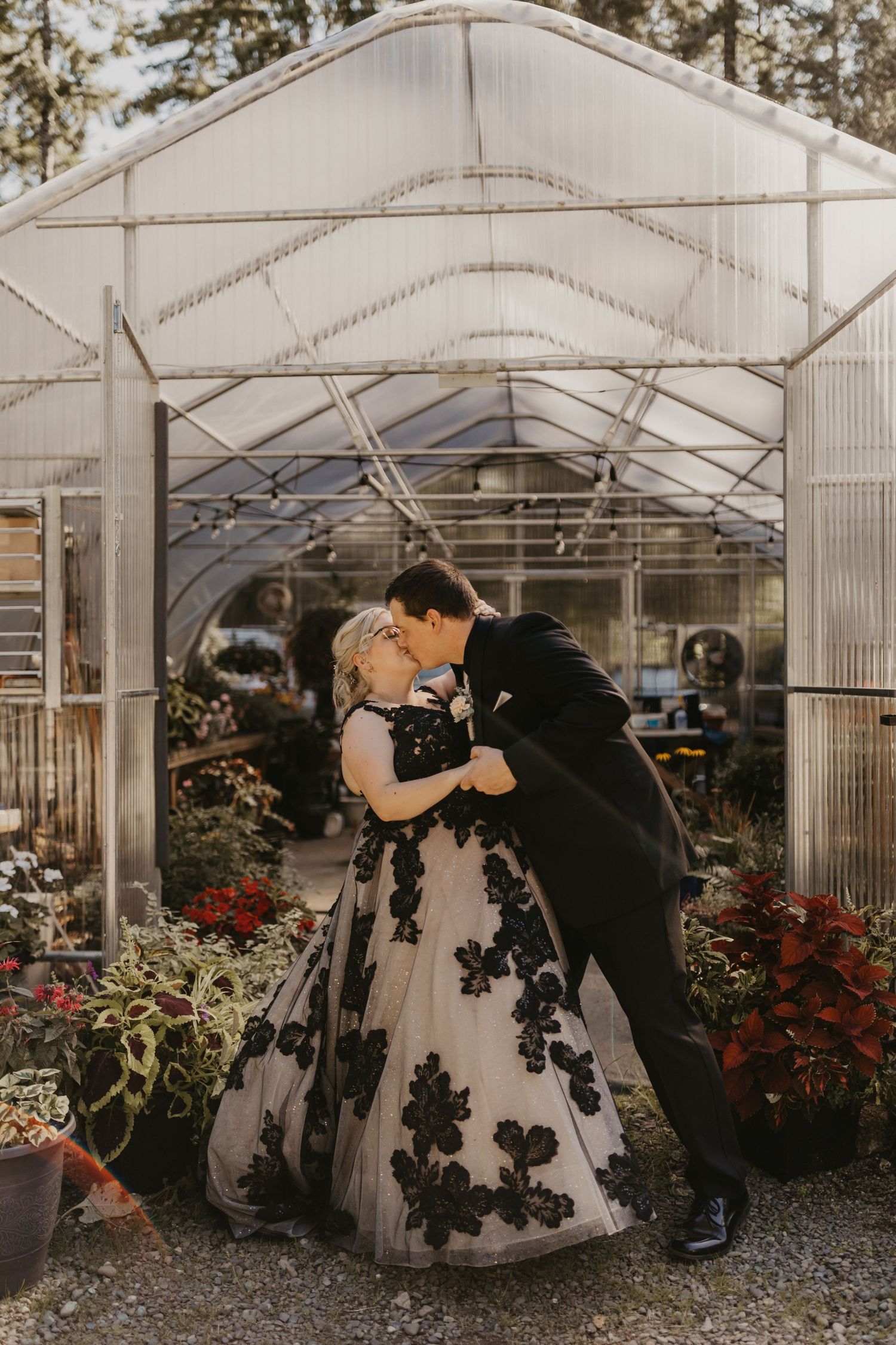 Romantic couple sharing a kiss in a greenhouse surrounded by flowers and natural light.