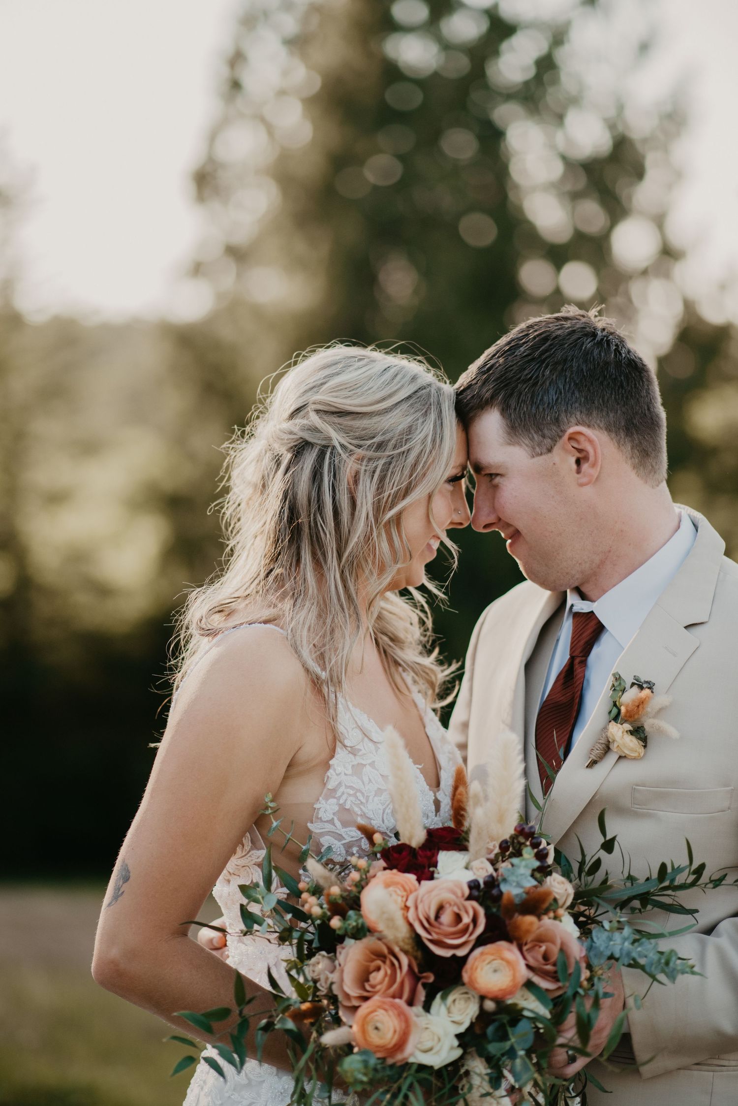 A couple shares an intimate moment with a beautiful bouquet of peach and burgundy flowers.