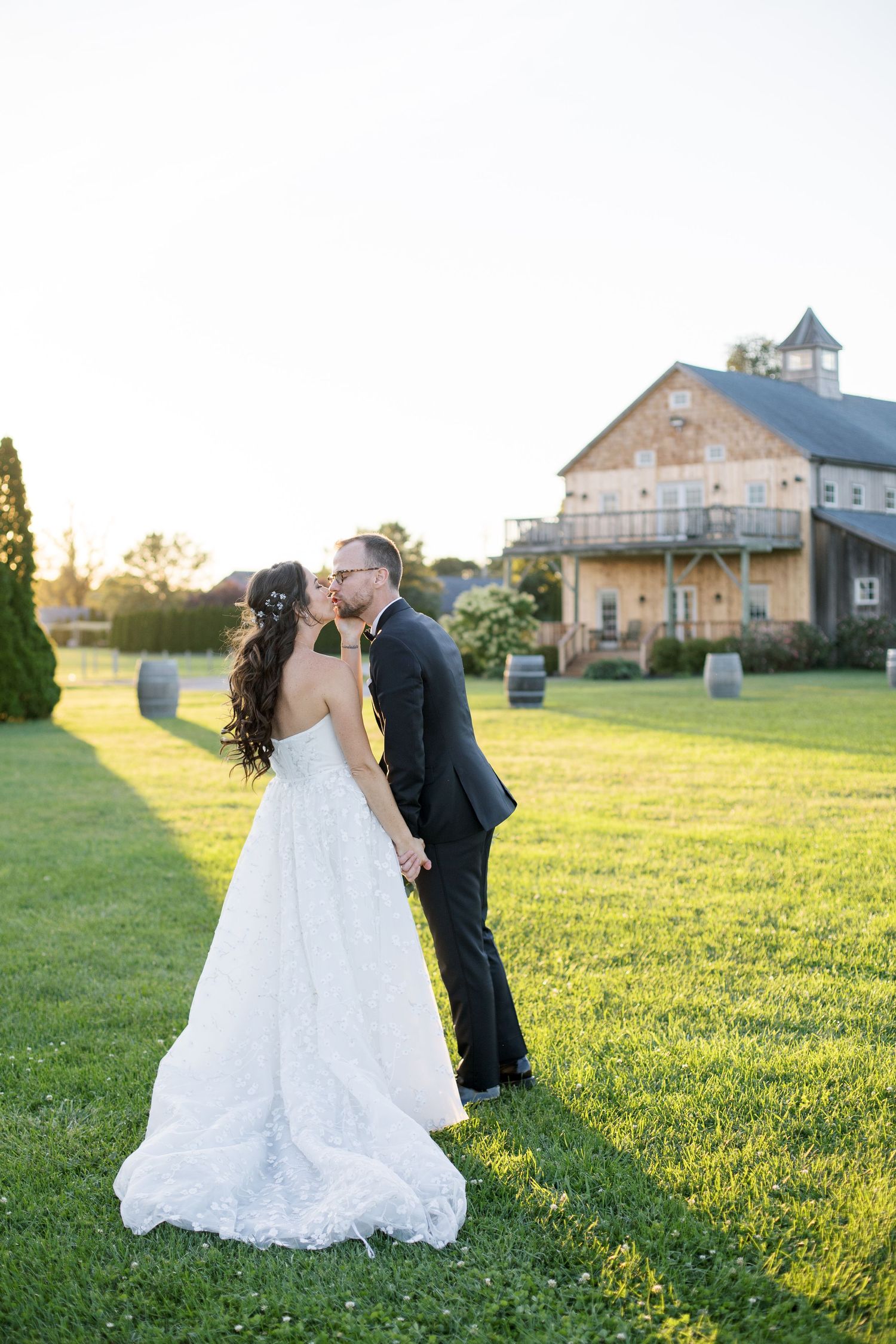 Romantic sunset kiss with rustic barn venue in background on manicured lawn.