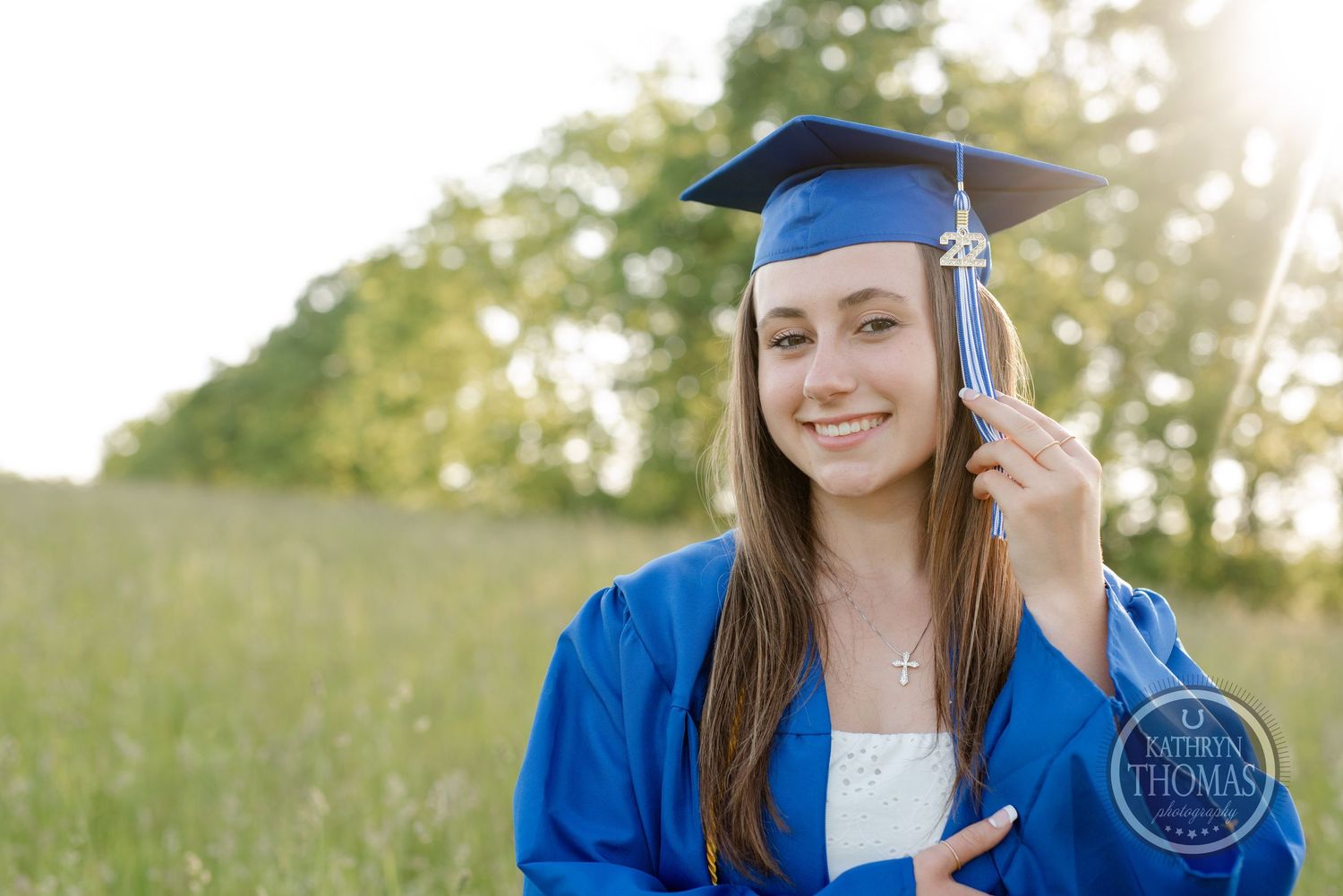 Graduation portrait in bright blue cap and gown against natural outdoor setting.