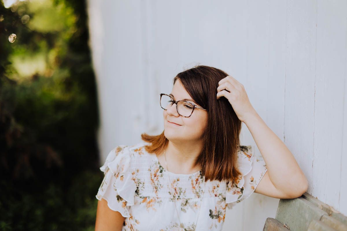Person in floral top posing against white wall outdoors.