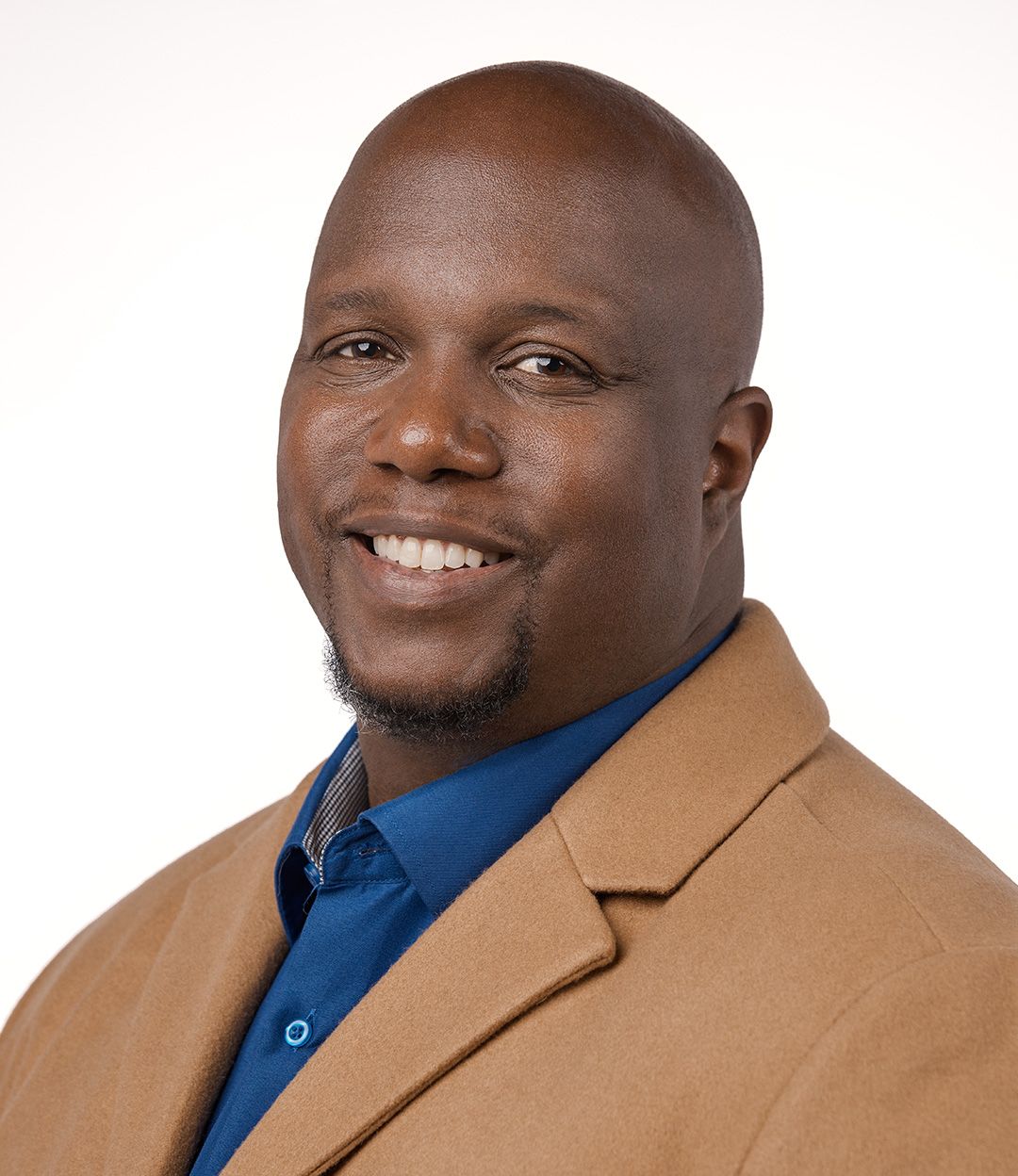 Professional portrait of person in tan blazer and blue shirt with warm smile.