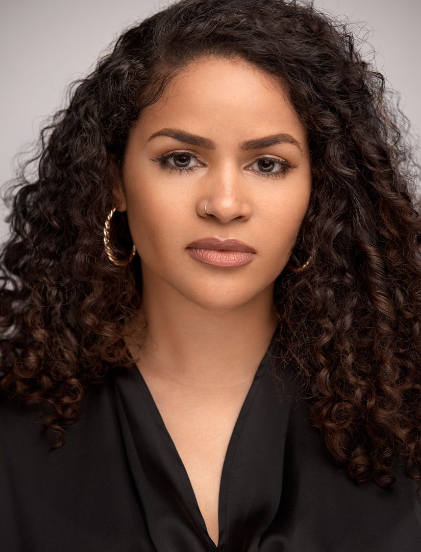 Studio portrait of person with curly hair wearing black top and hoop earrings.