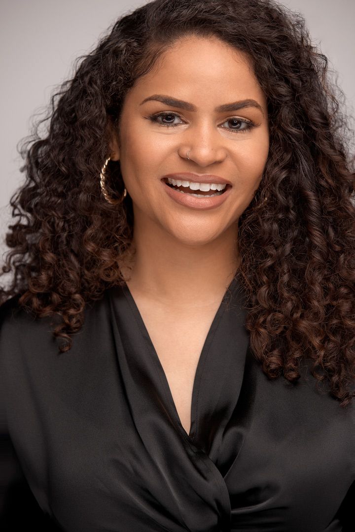 Professional headshot of person with natural curly hair and black wrap top.