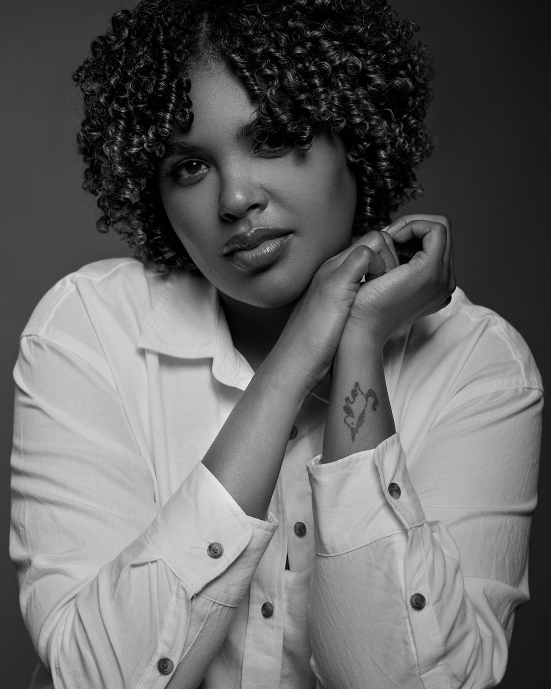 Artistic black and white portrait with natural curls and relaxed pose in white button-down.