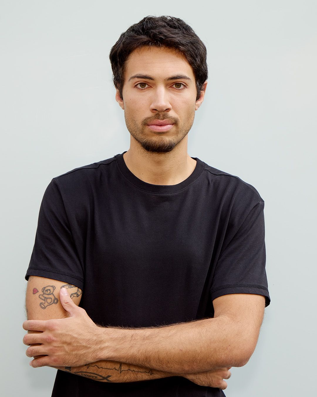 Studio portrait of person wearing black t-shirt with crossed arms showing tattoos.