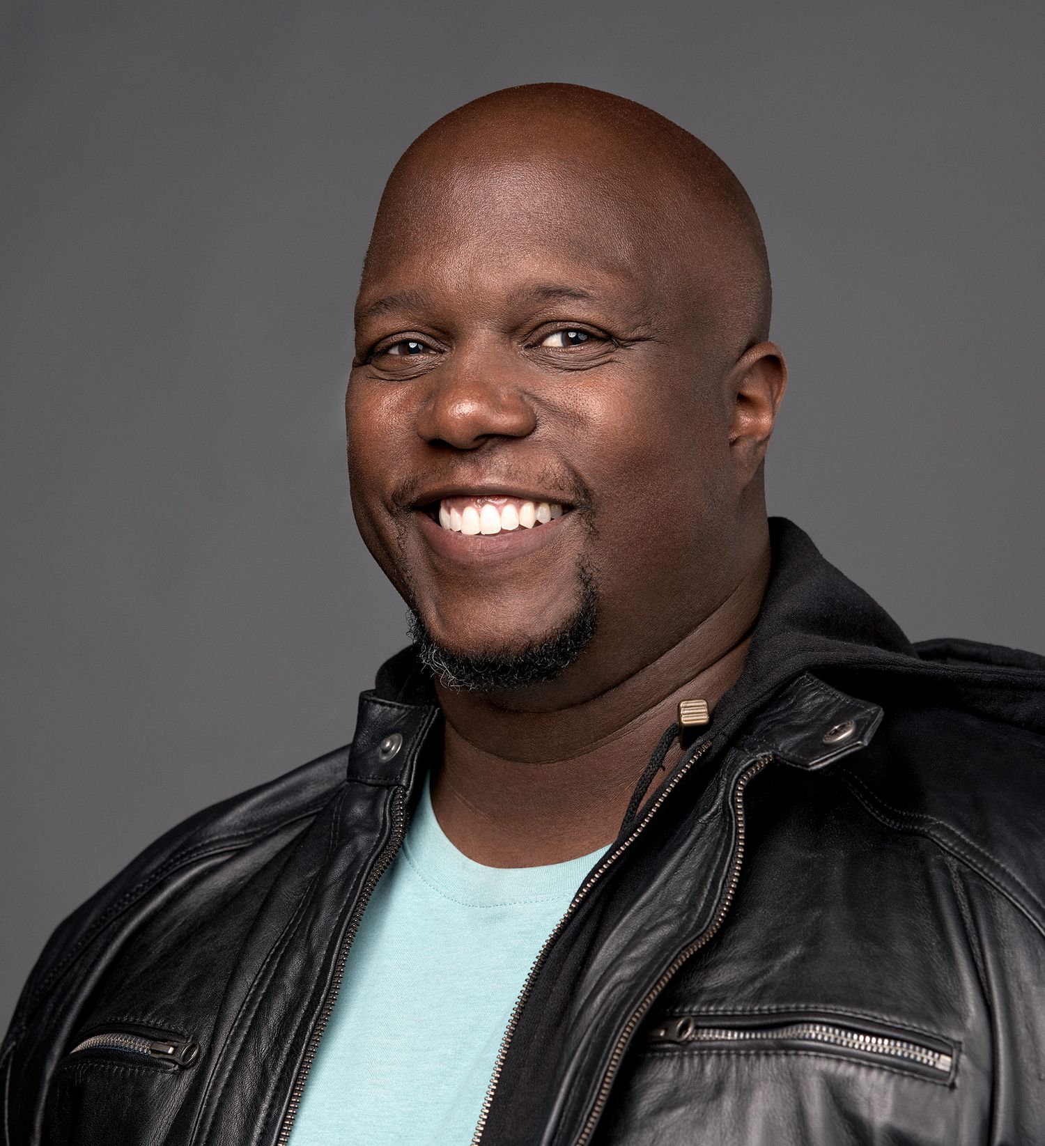 Casual portrait of person in leather jacket and mint green shirt with bright smile.
