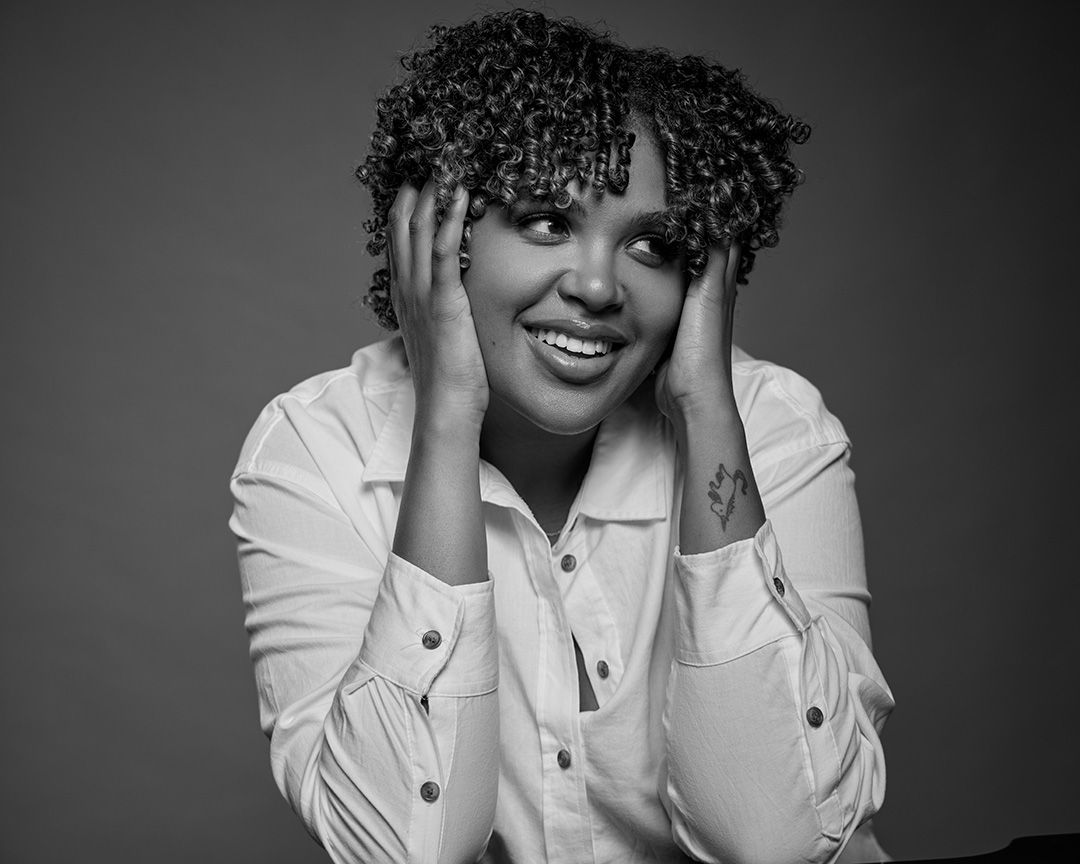 Black and white portrait showing joyful expression with hands framing face in white button-down shirt.
