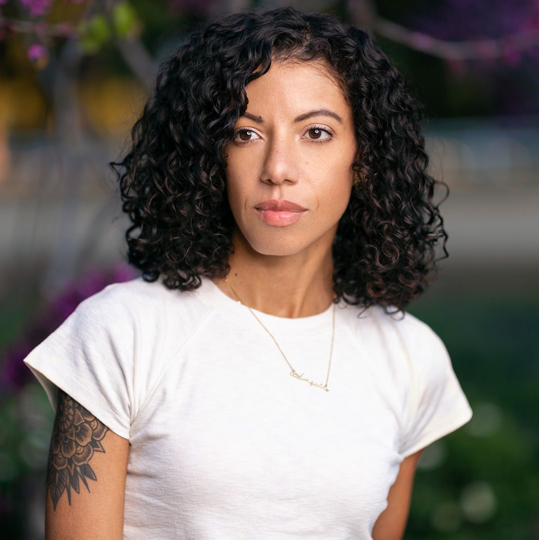 Portrait of person with curly hair wearing white t-shirt and delicate necklace.