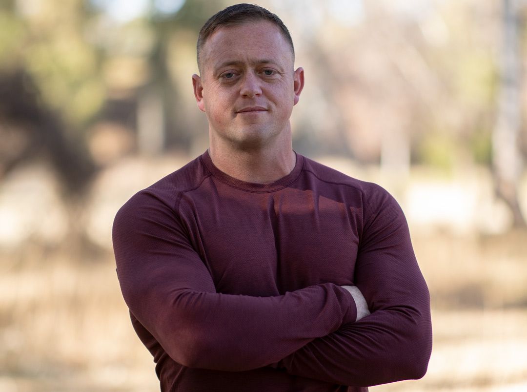 Portrait of a person in a burgundy long-sleeve shirt outdoors with trees in background.