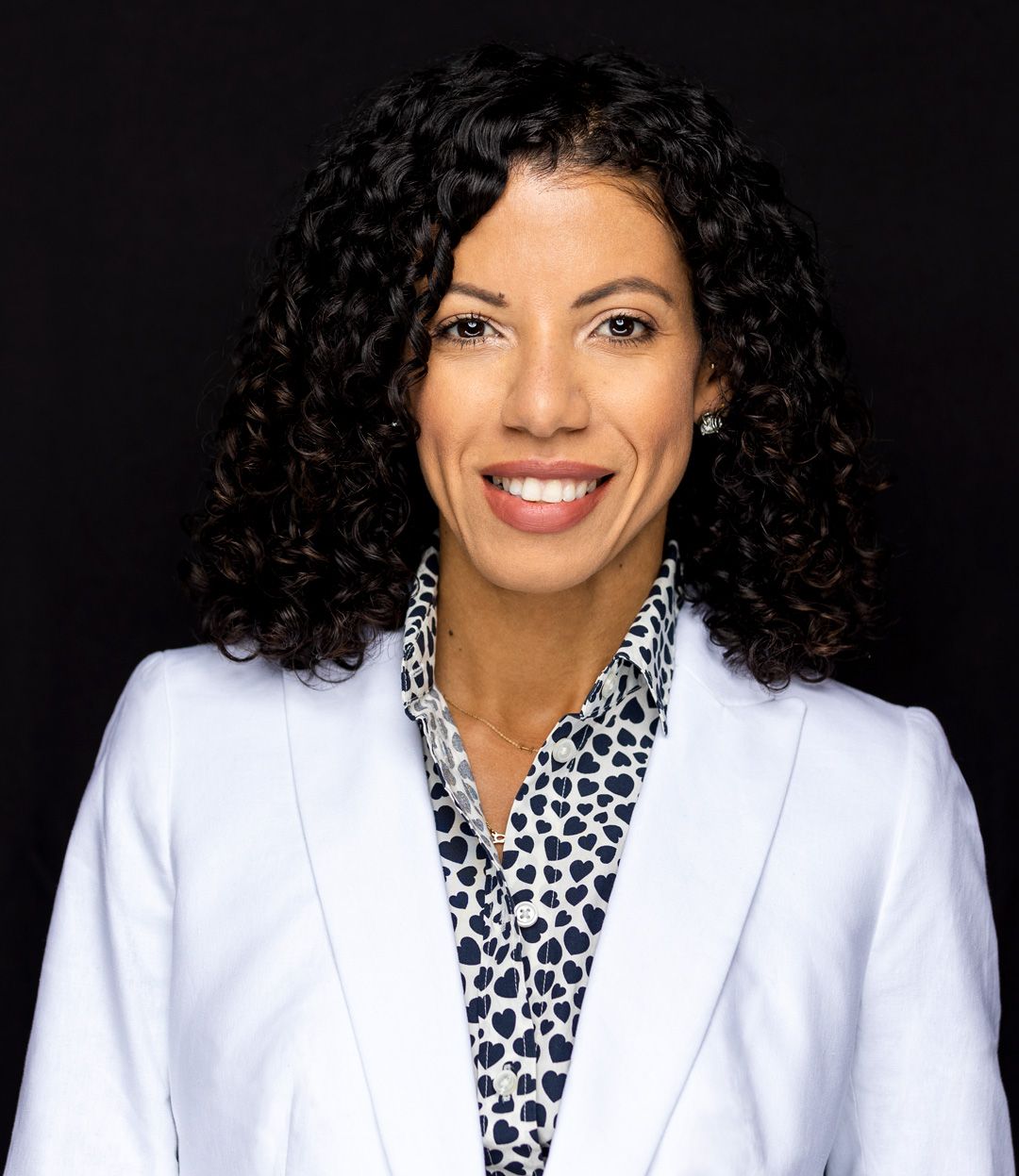 Professional headshot of a person in white blazer and animal print blouse with curly hair.