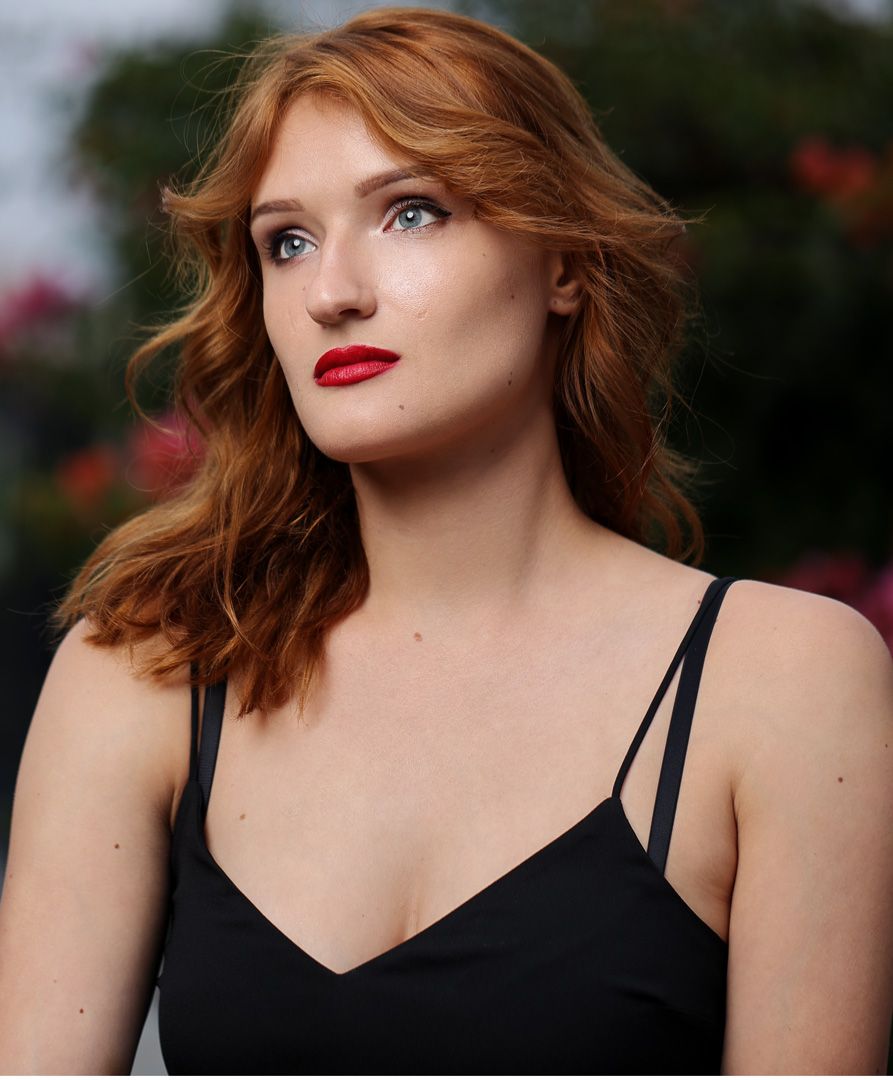 Elegant portrait of a person with red hair and lipstick wearing a black dress.