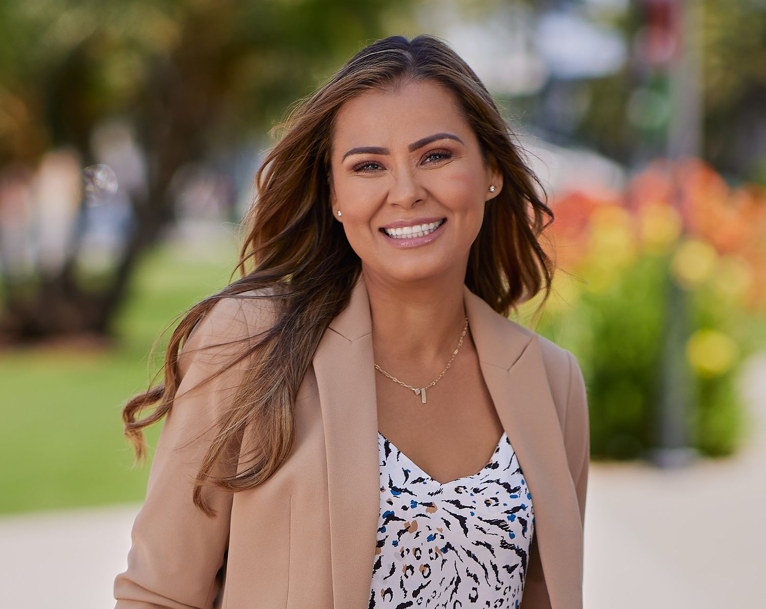 Outdoor portrait of a person in beige blazer and patterned top smiling at camera.