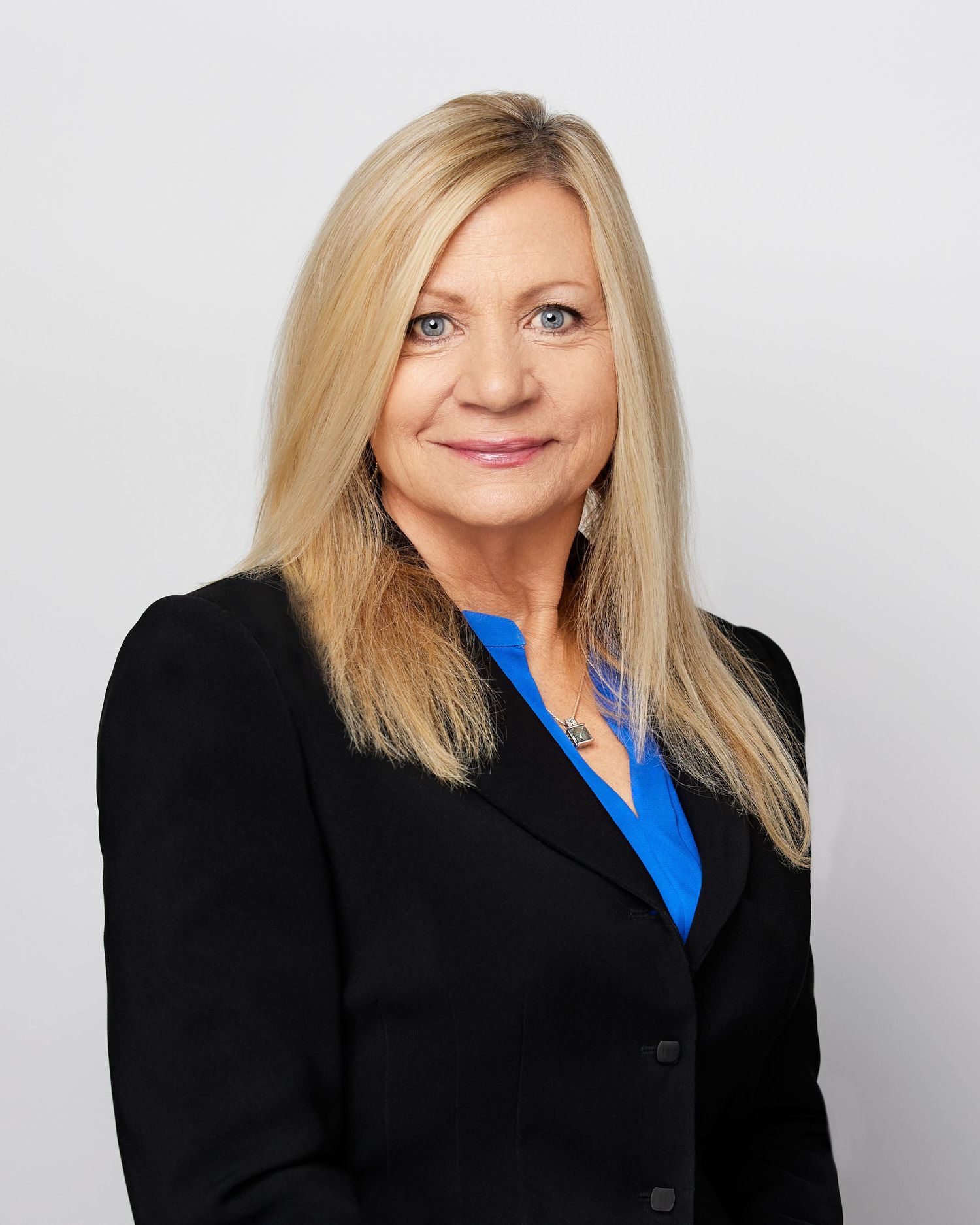 Professional headshot of a person in black blazer and blue blouse against grey background.