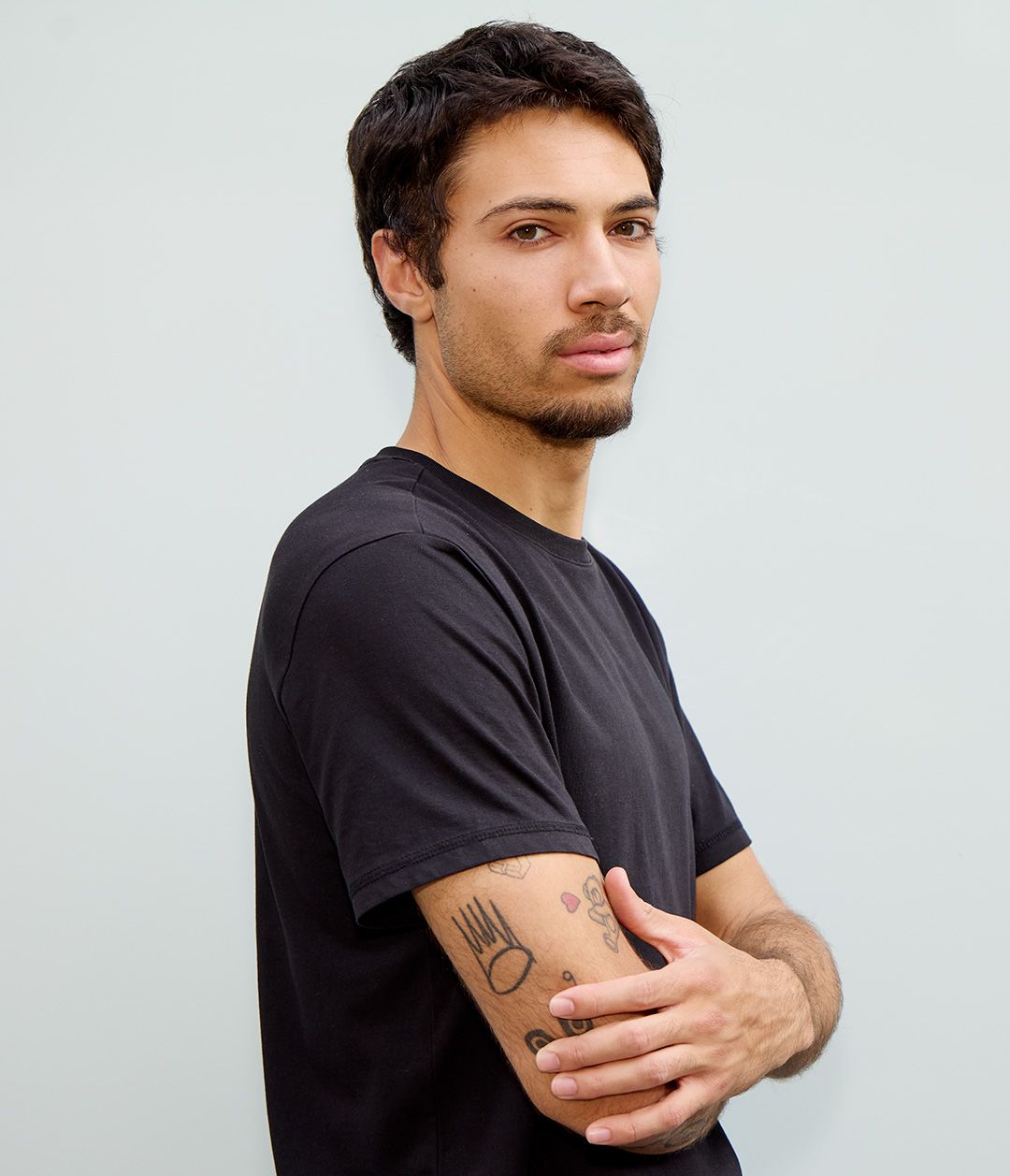 Professional headshot of person in black t-shirt with visible arm tattoo against light background.