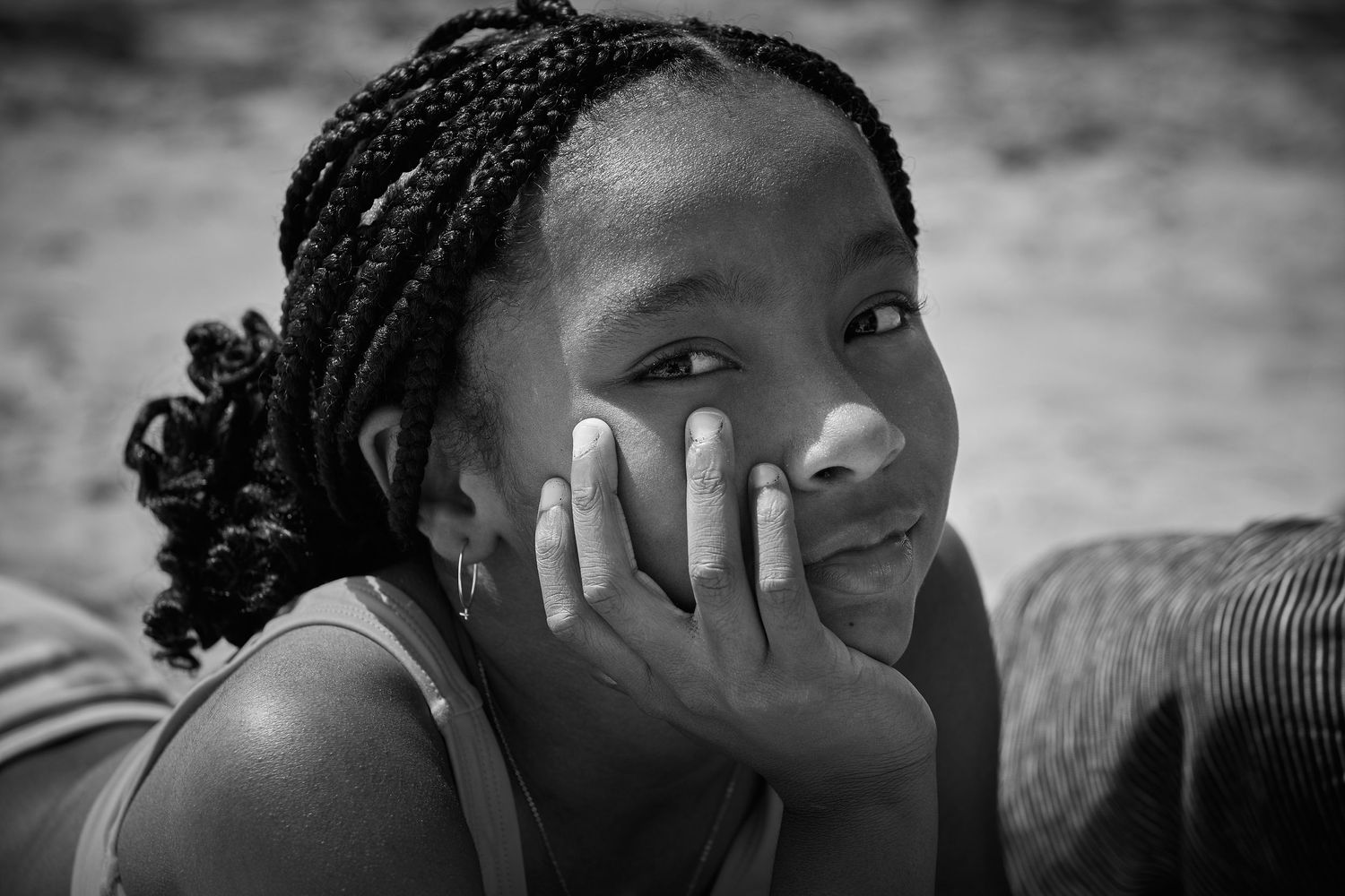 Black and white portrait of a young person with braided hair resting their head on their hand.