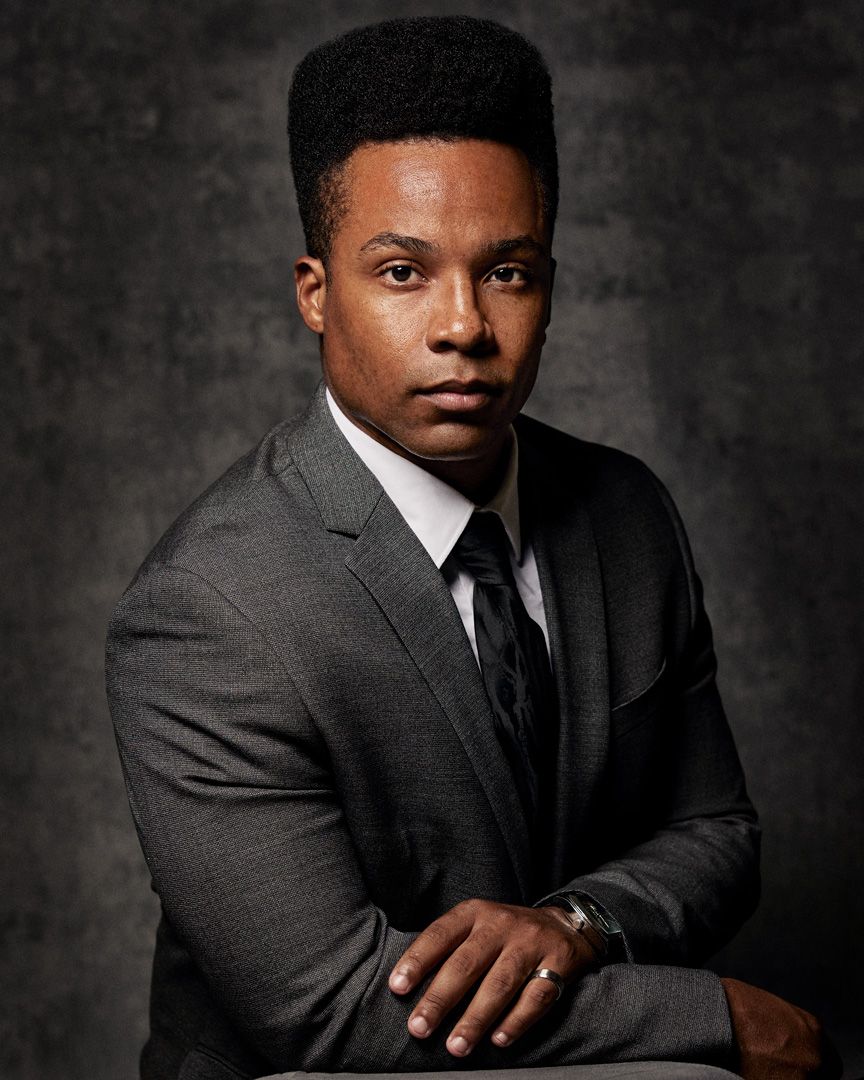 Professional headshot portrait in grey suit against textured dark background.