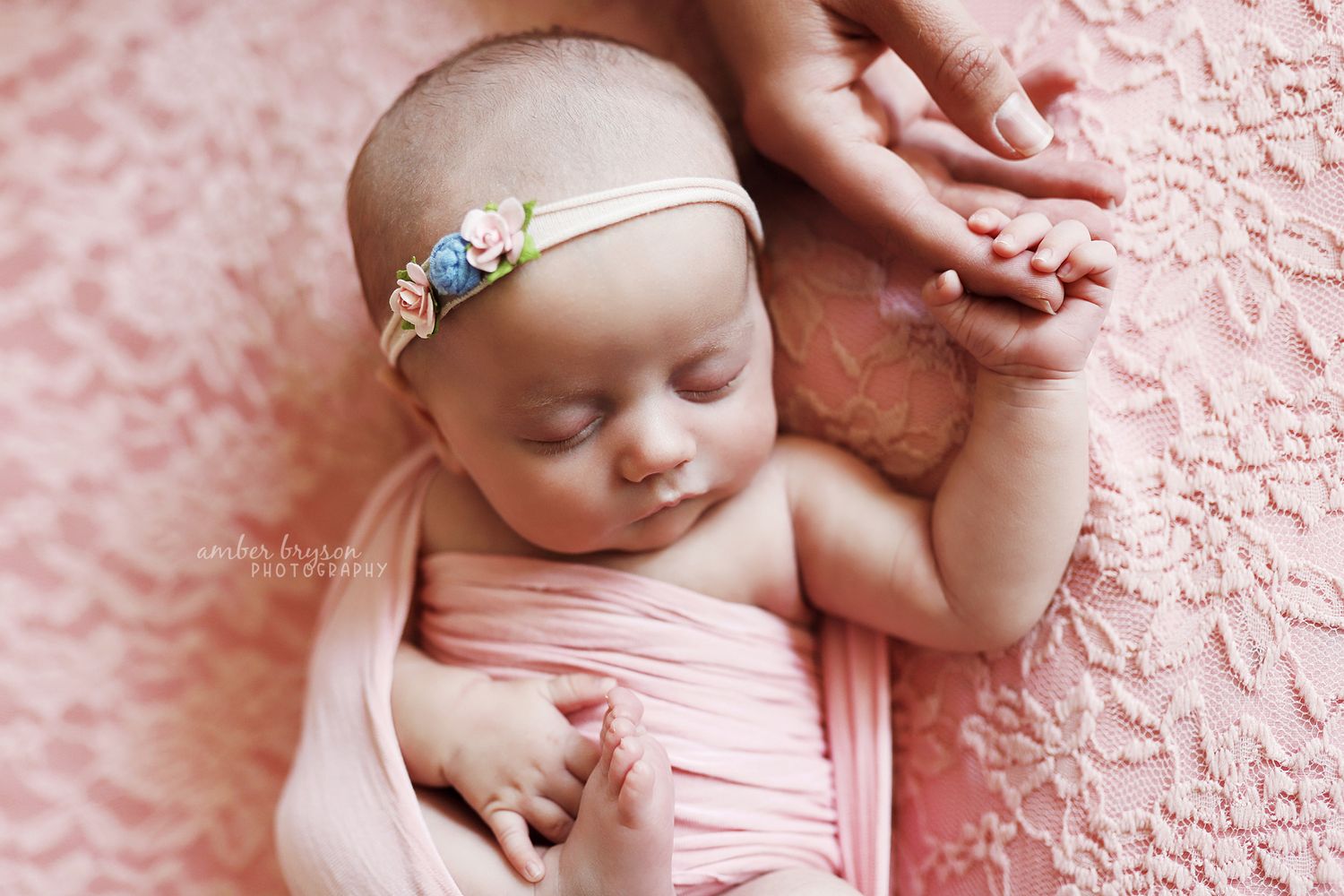 Sleeping newborn in pink wrap on textured pink background with delicate headband.
