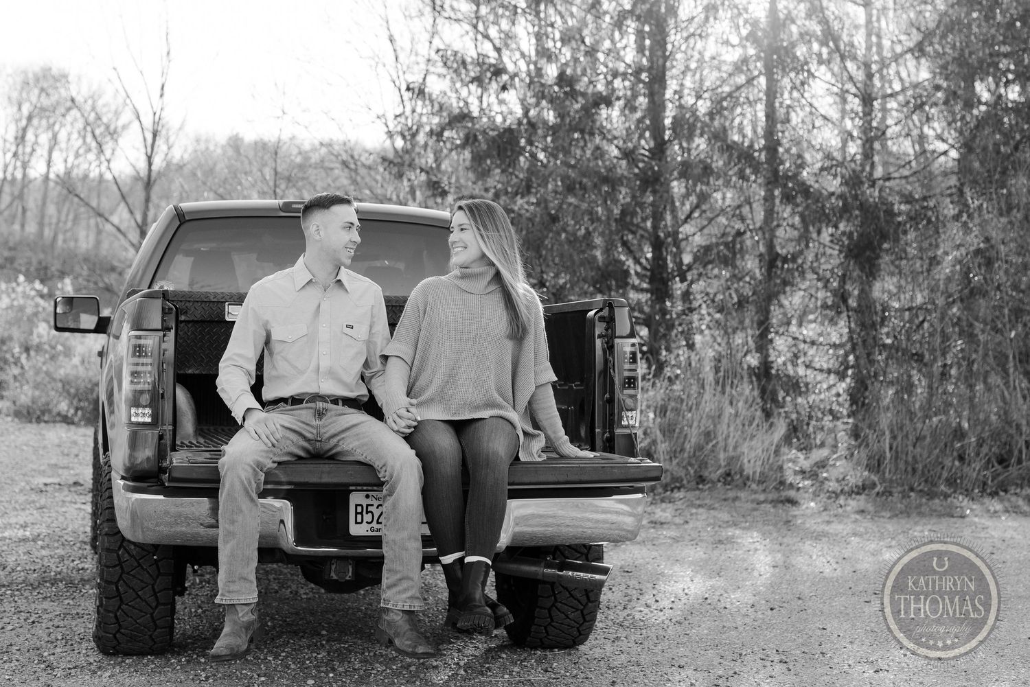 Black and white portrait of a couple sitting on the tailgate of a pickup truck.