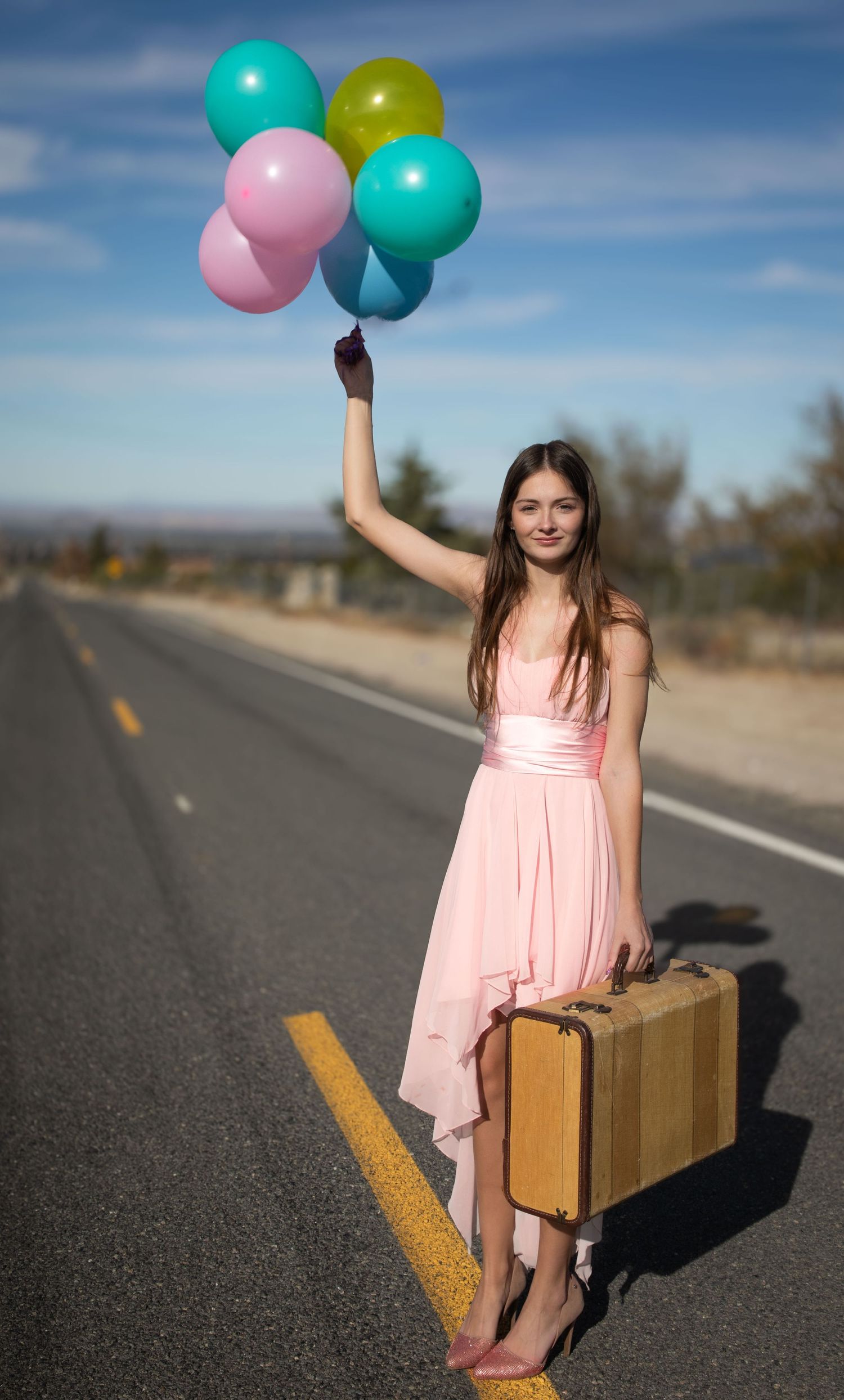 Girl holding balloons and a suitcase