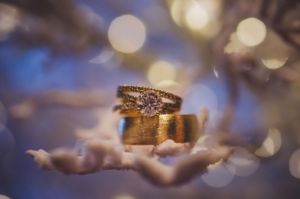 Close-up of diamond engagement ring and gold wedding band with bokeh light background.