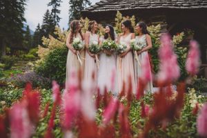 Bridesmaids in blush gowns holding bouquets surrounded by vibrant pink flowers in garden.
