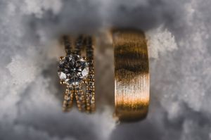 Diamond engagement ring and gold wedding band nestled in snow for stunning jewelry detail shot.