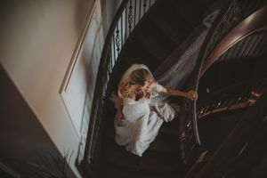 Aerial view of bride in white gown descending ornate wooden staircase in vintage venue.