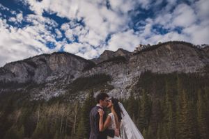 Couple shares a romantic kiss beneath stunning mountain cliffs and dramatic cloudy skies.