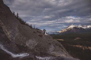 Wedding couple embraces on a rugged mountain ridge with sweeping valley views below.