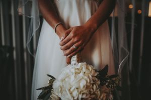 Close-up of bride's hands adorned with a diamond ring resting on a white hydrangea bouquet.