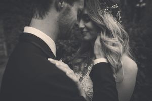 Black and white romantic photo of bride and groom sharing a tender moment in wedding attire.