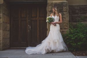Stunning bride in ruffled mermaid wedding dress holds bouquet while posing before ornate wooden doors.