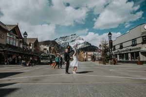 Wedding couple crossing a street in downtown Banff with snow-capped Rocky Mountains in the background.