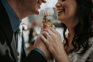 Newlywed couple laughing while sharing an ice cream cone, bride showing off diamond engagement ring.