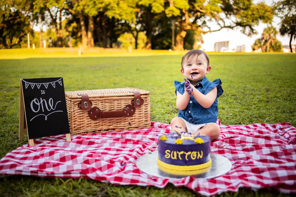 Baby girl celebrating first birthday with a smash cake at a park picnic.