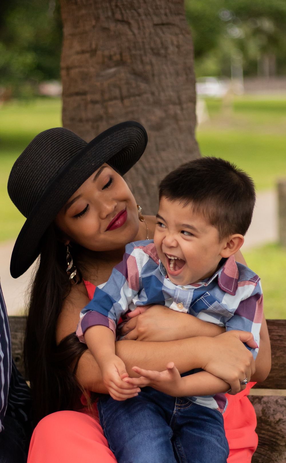 Laughing toddler boy being held by his stylish mother in a park.