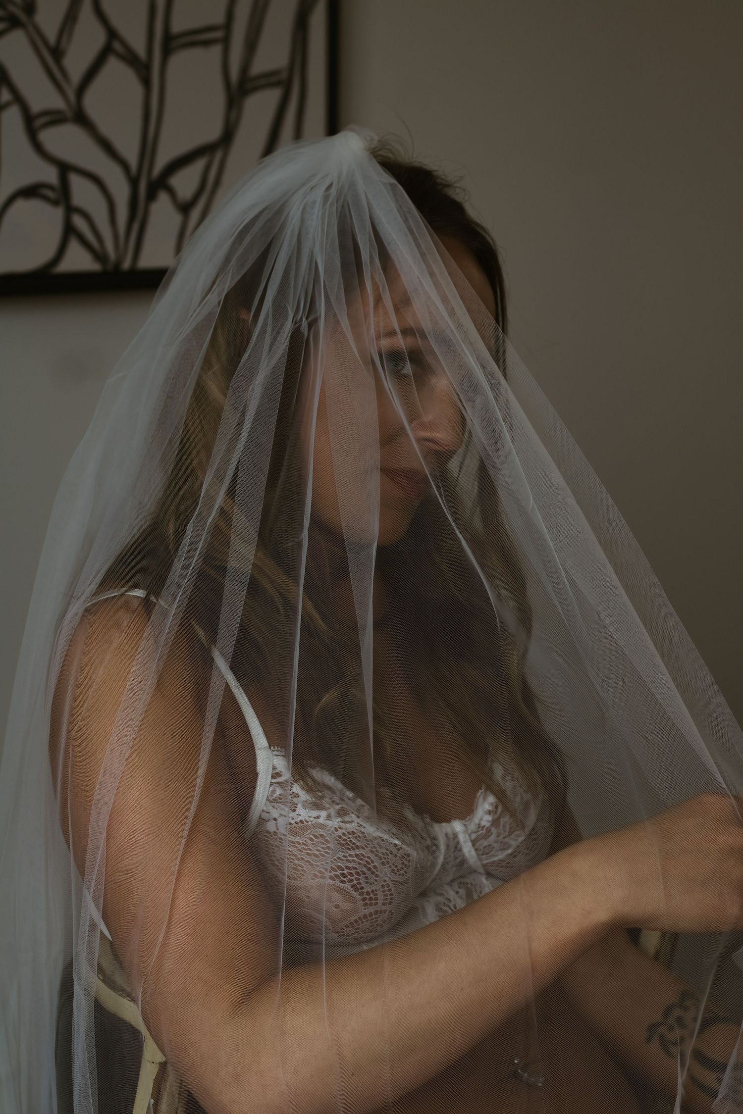 Bride wearing delicate lace lingerie poses beneath flowing wedding veil.