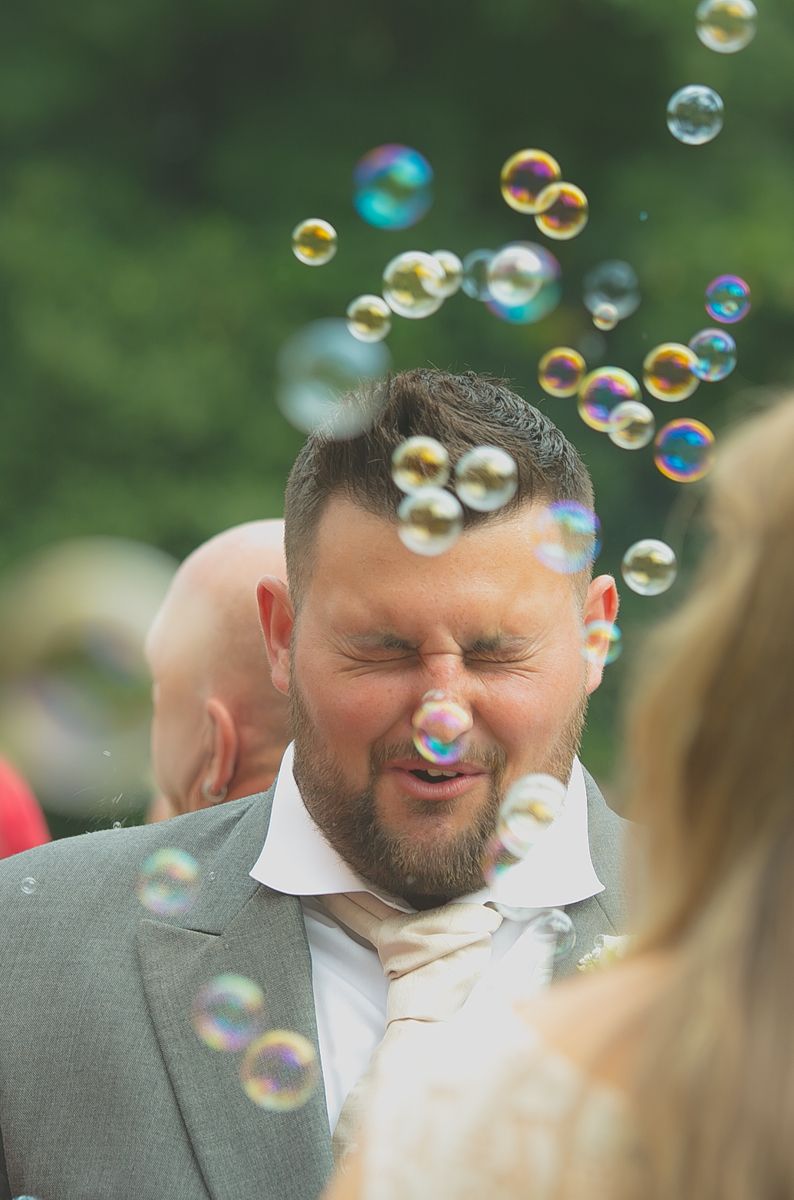 Bubbles blow in front of the best man's face during a wedding reception