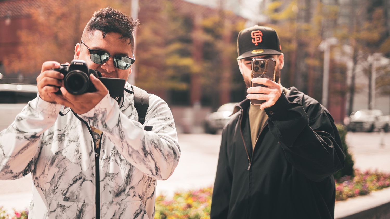 Two photographers taking pictures in an urban setting during fall.