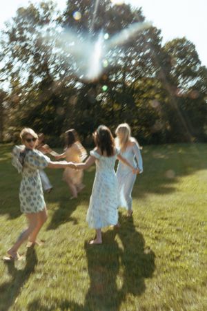 People in light summer dresses dancing and twirling in a sunny field.