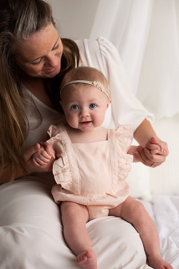 Six month old baby girl sitting on mom's lap smiling.
