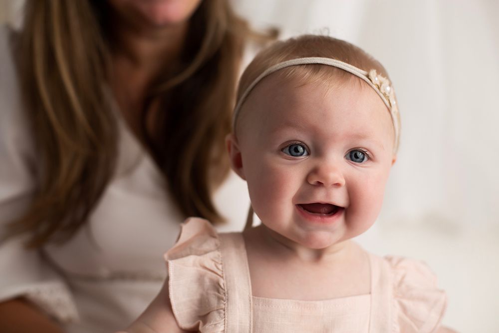 Six month old baby girl headshot of her smiling at the camera.