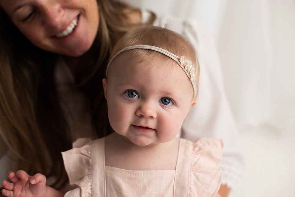 Six month old baby girl sitting on mom's lap smiling at the camera.