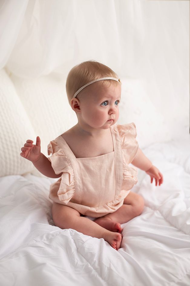 Six month old baby girl sitting in a pink romper looking slightly off camera.