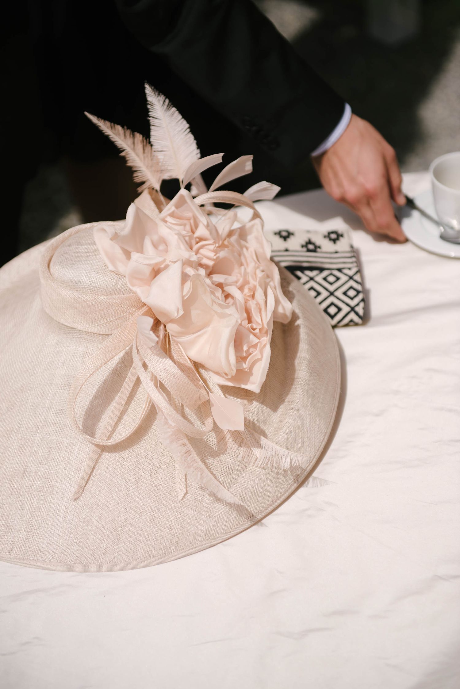 Elegant pale pink fascinator hat with feathers and floral details on white tablecloth.
