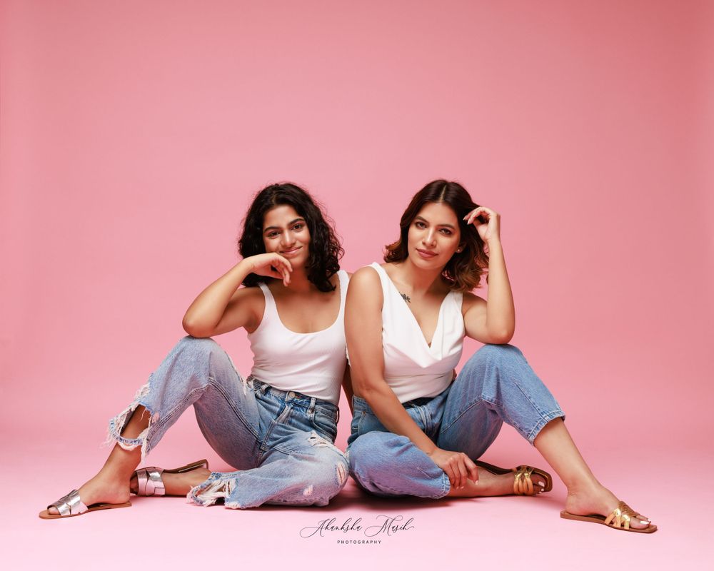 Casual portrait of two people in denim and white tops against pink backdrop.